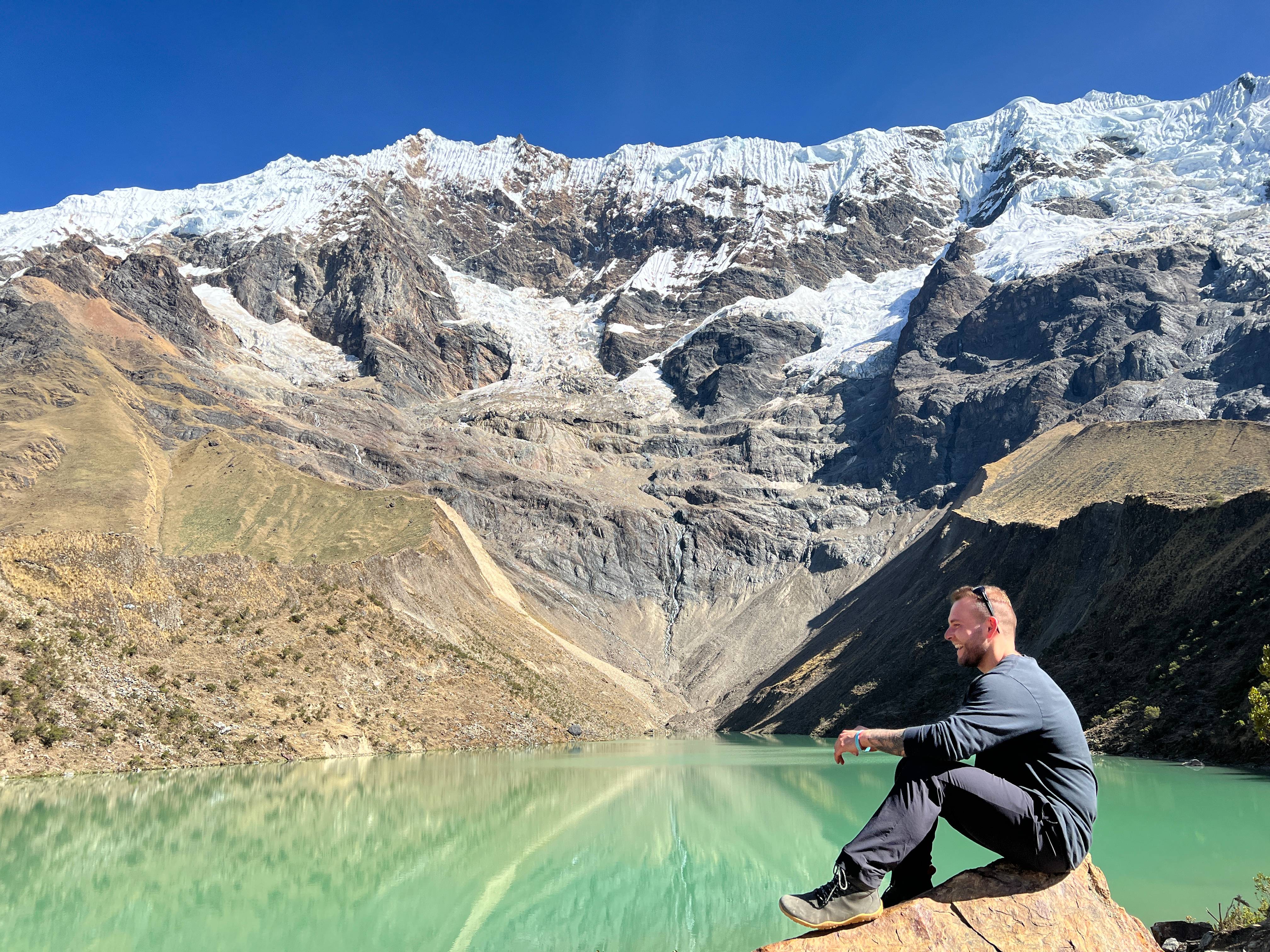 Person sitting by turquoise Humantay Lagoon with snow-capped mountains